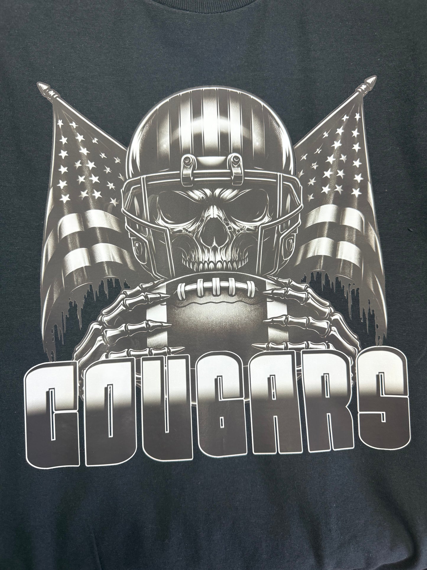 Black t-shirt with a graphic design of a skull in a football helmet with American flags and the word 'COUGARS'.